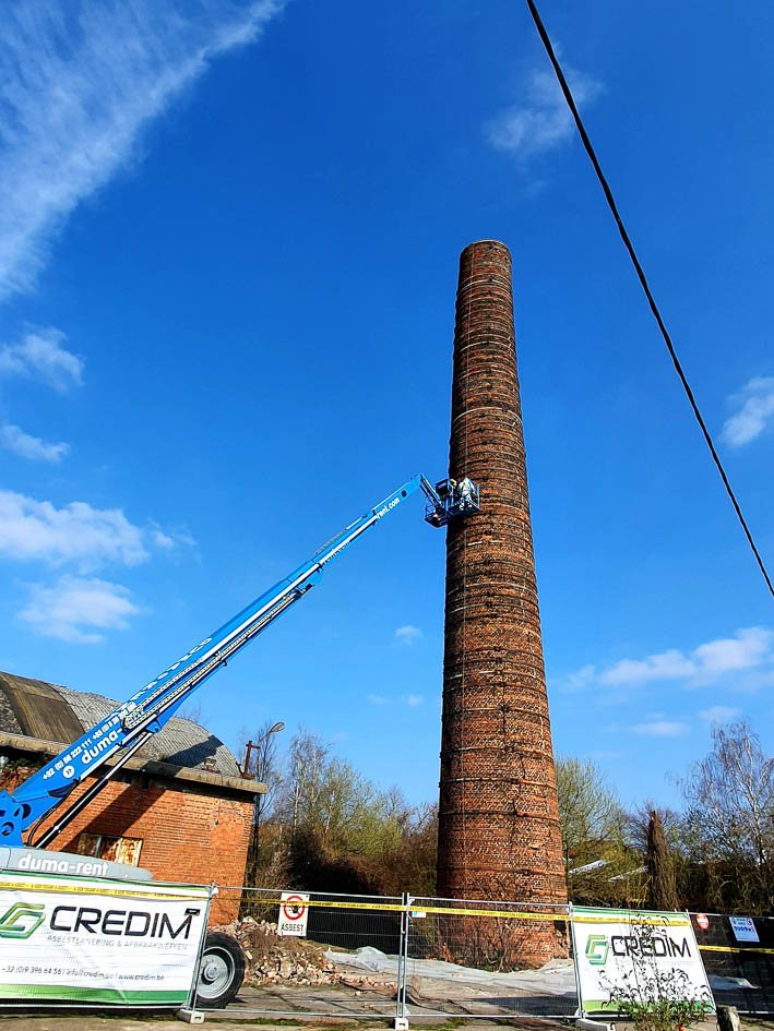 Work on a factory chimney with an aerial platform, Credim banners on the fence