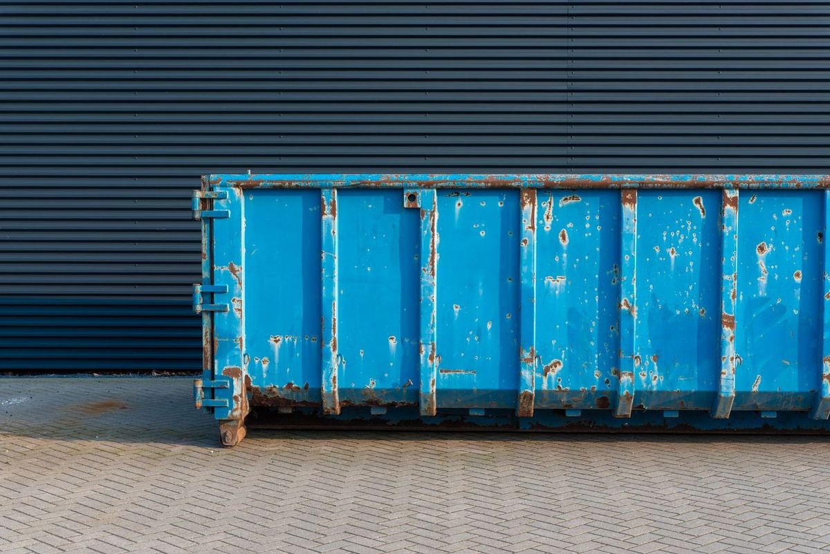 Roestige blauwe container op klinkers voor een donkere metalen gevel