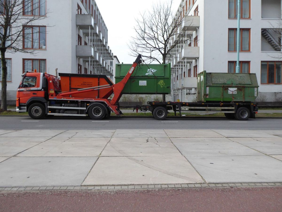 Camion à bras de levage avec deux conteneurs verts dans une rue