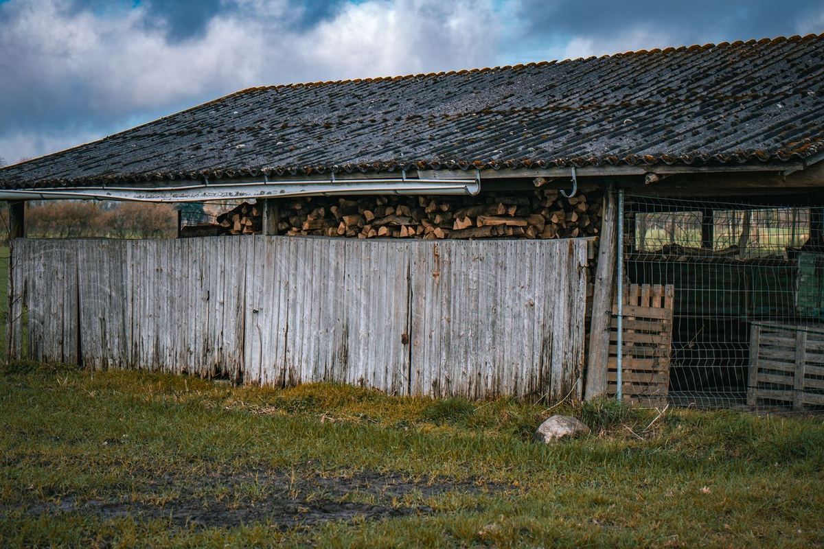 Ancien hangar en bois avec un toit en plaques ondulées et du bois de chauffage empilé