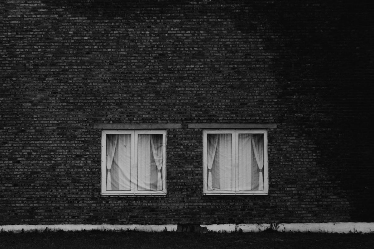 Dark brick wall with two curtained windows, in black and white
