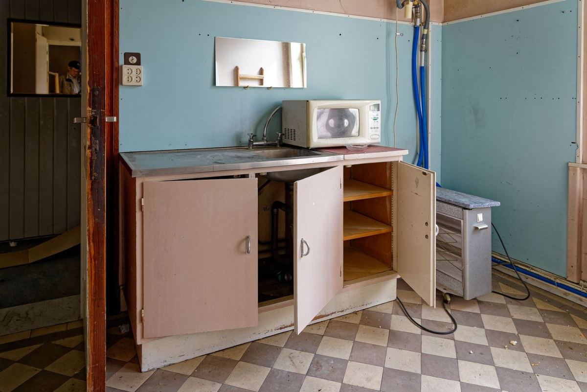 Cuisine abandonnée avec placards ouverts et sol en damier