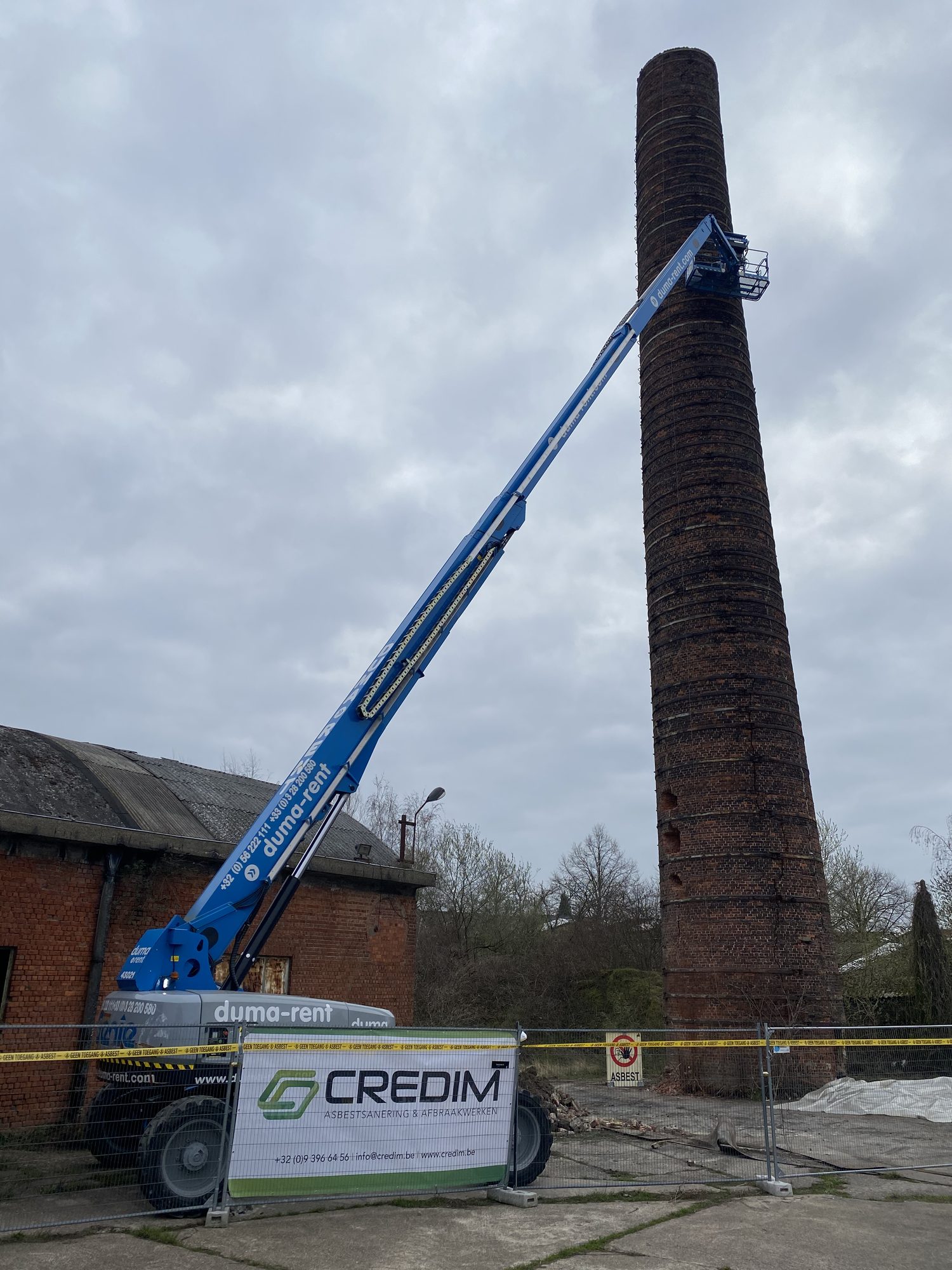 Nacelle élévatrice contre une haute cheminée en briques lors du retrait de mastic