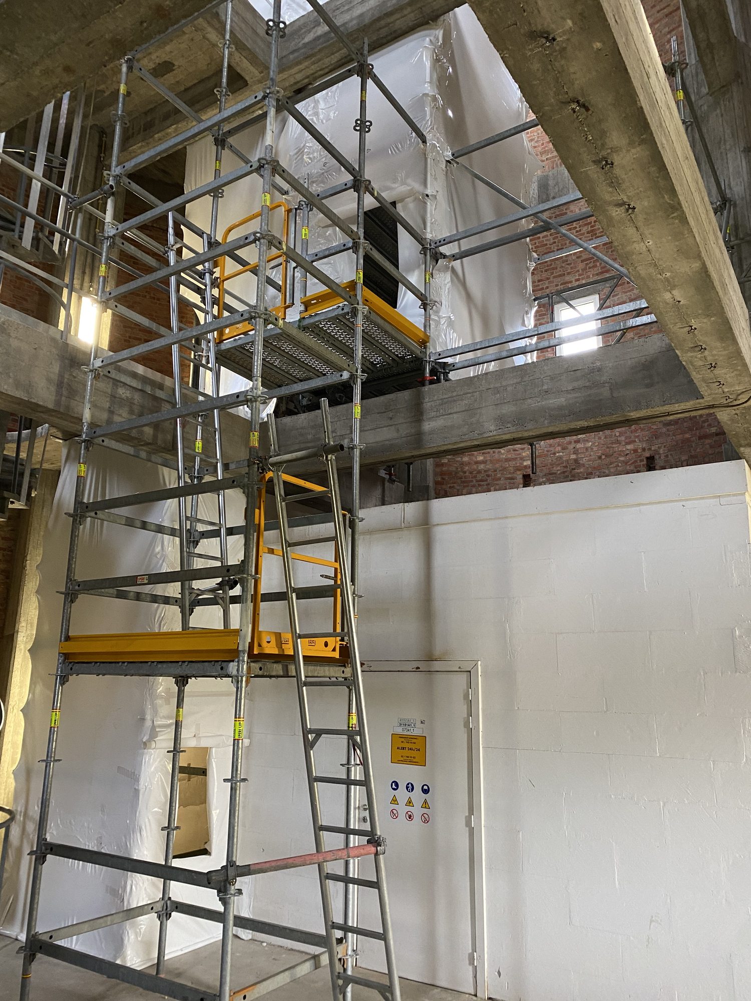 Scaffolding next to a hermetic zone of white plastic sheeting in an industrial building
