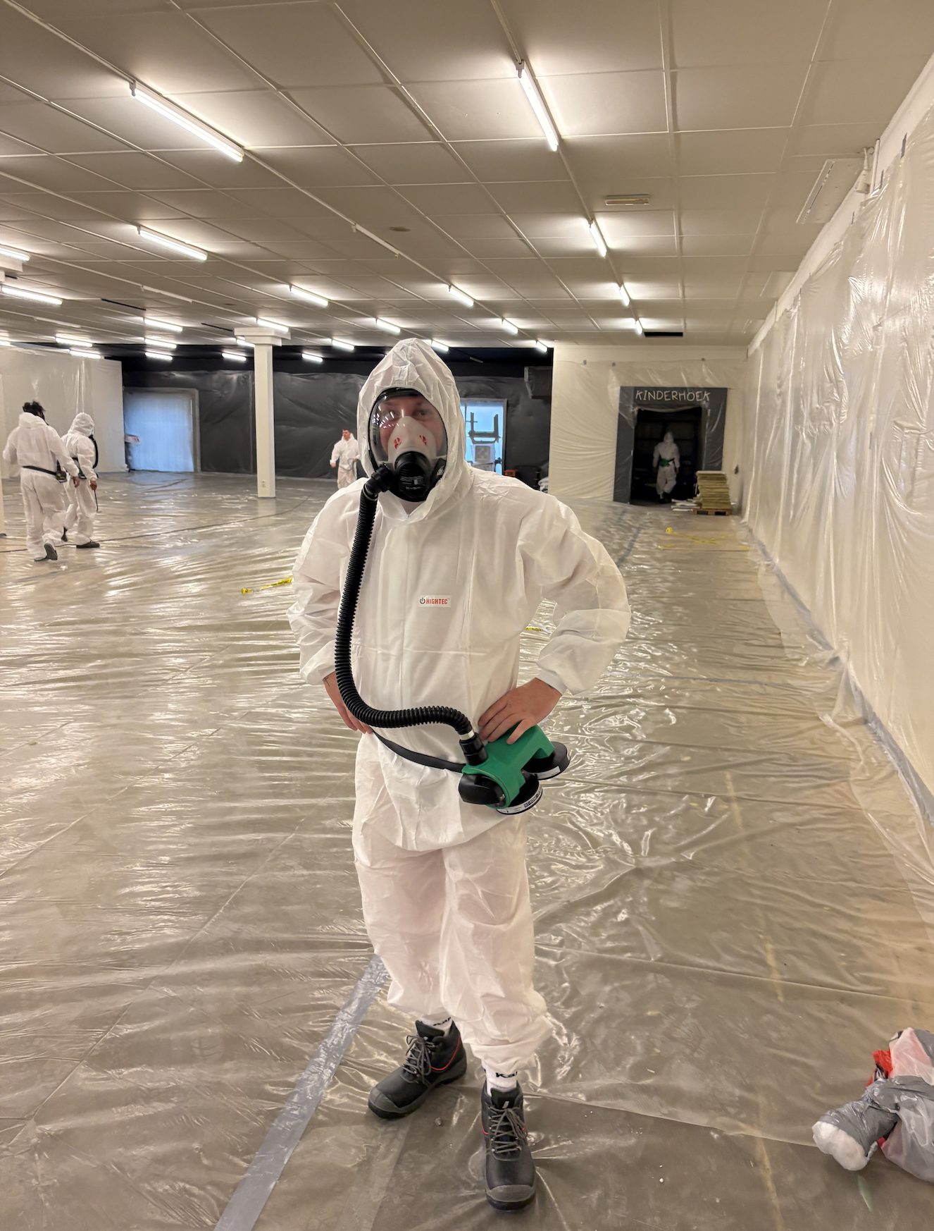 Worker in a disposable coverall with respiratory protection in an area screened off with plastic sheeting