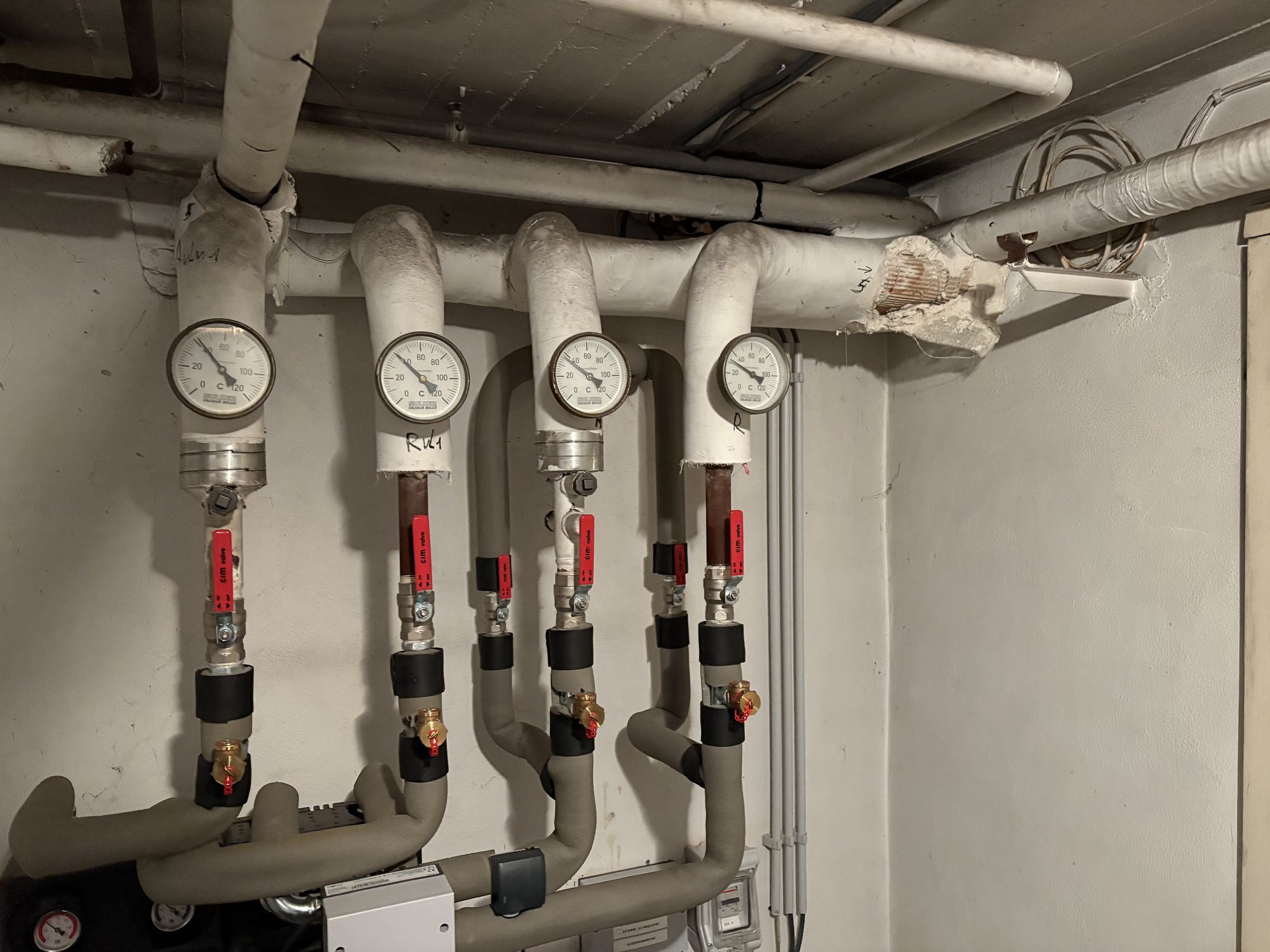Insulated pipes with four dial thermometers in a plant room