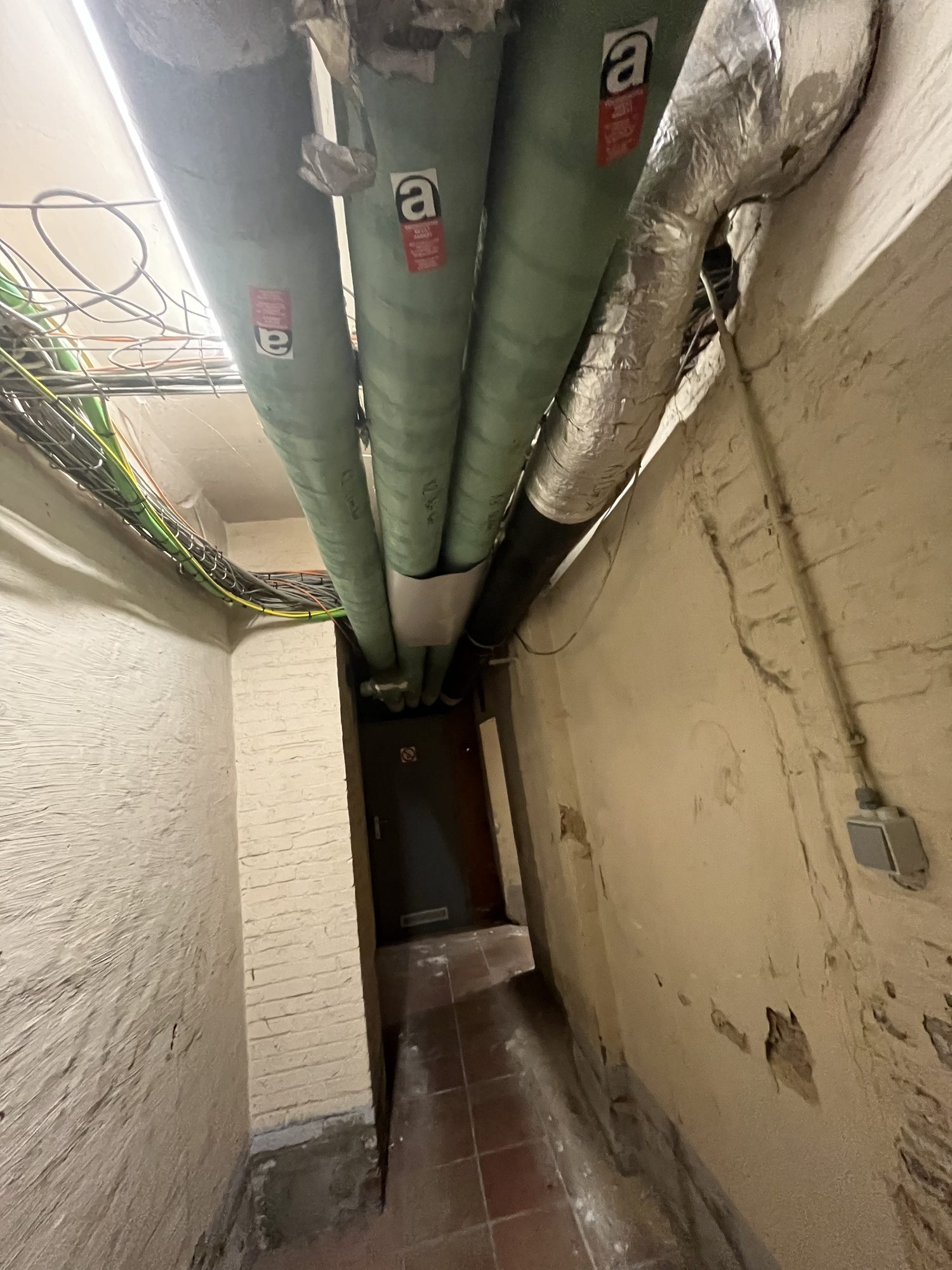 Green pipes with asbestos warning stickers in a narrow corridor
