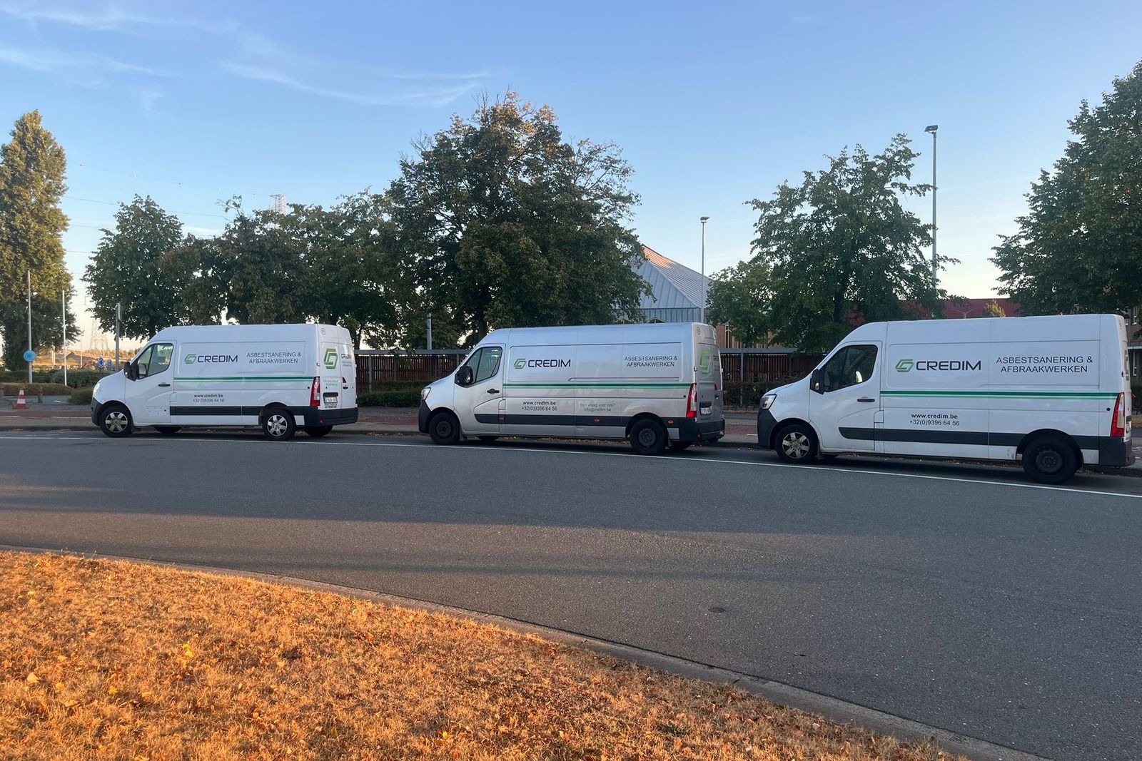 Drie bestelwagens van Credim geparkeerd langs een weg met bomen