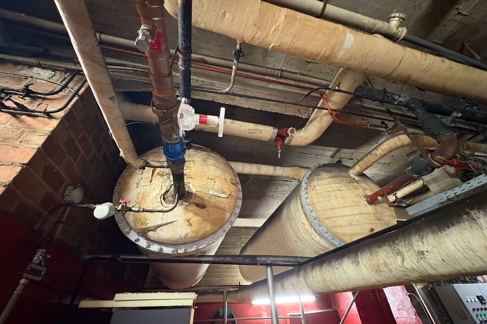 Pipes and two cylindrical vessels with insulation under a ceiling, seen from below