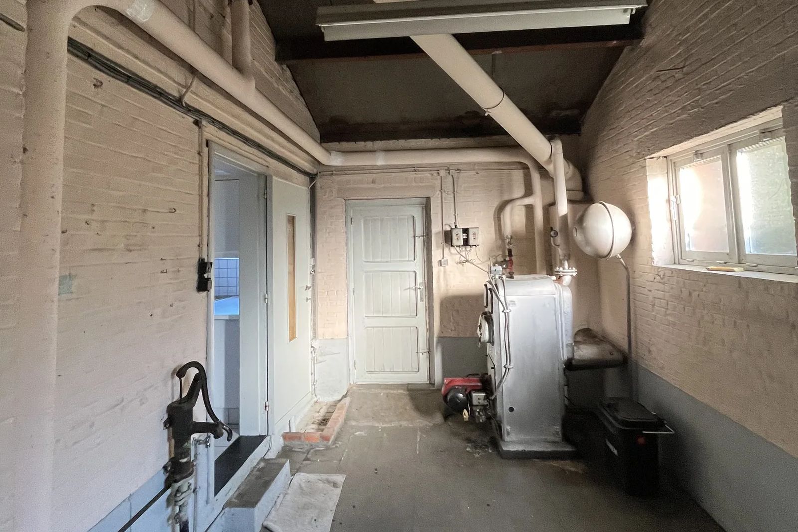 Local avec une chaudière et des conduites isolées blanches le long des murs et du plafond