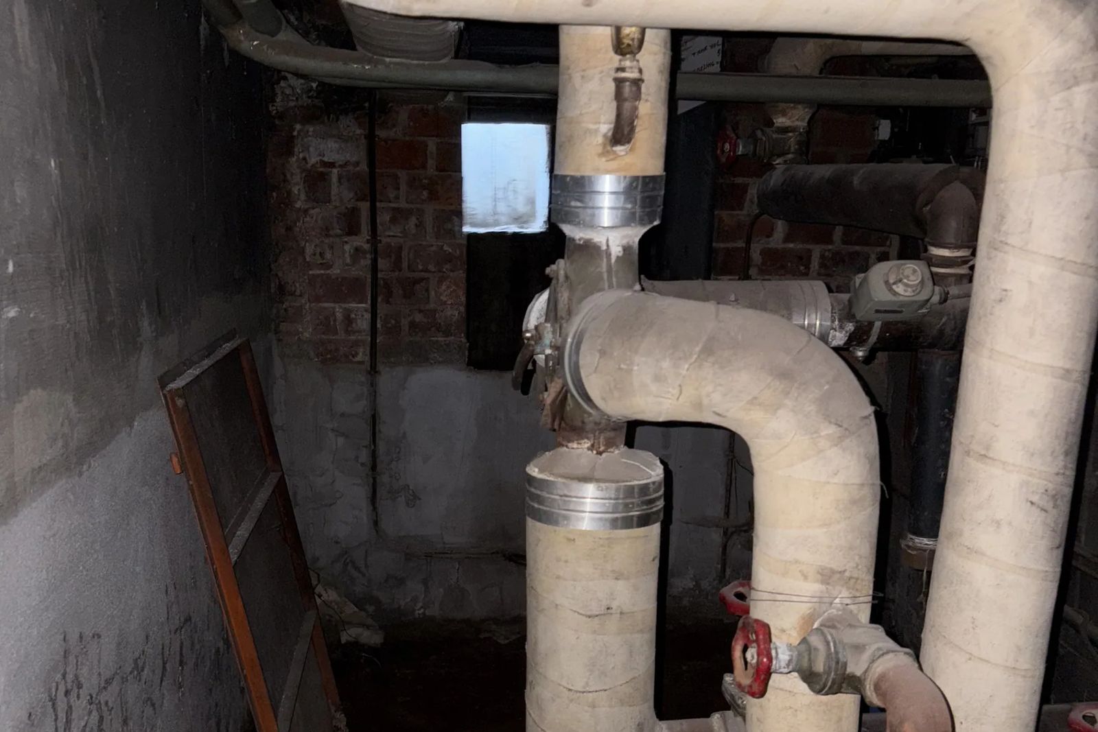 White insulated pipes with red-handled valves in a dark room with a brick wall