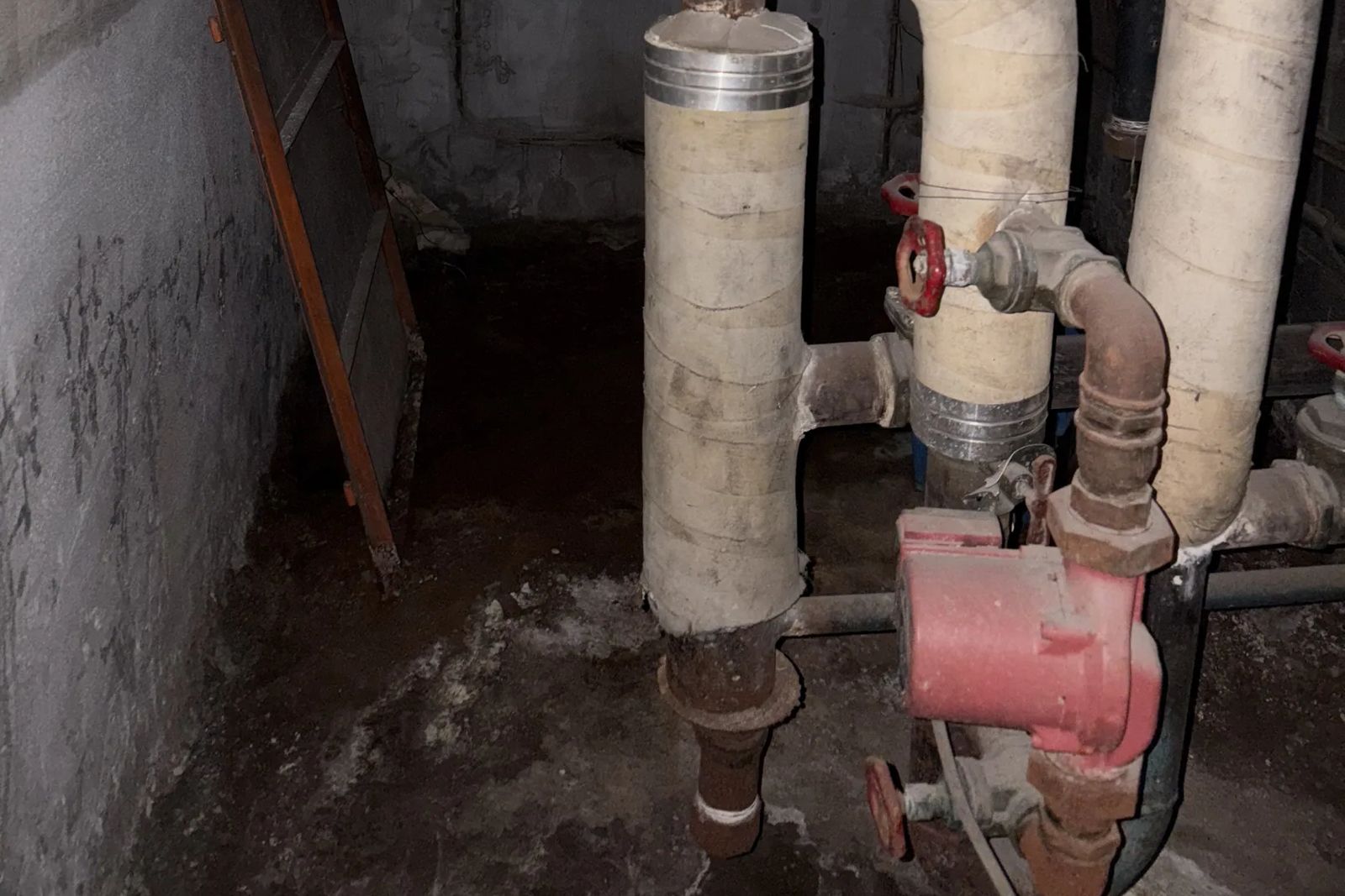 Insulated pipes with a red pump and red-handled valves in a dark room