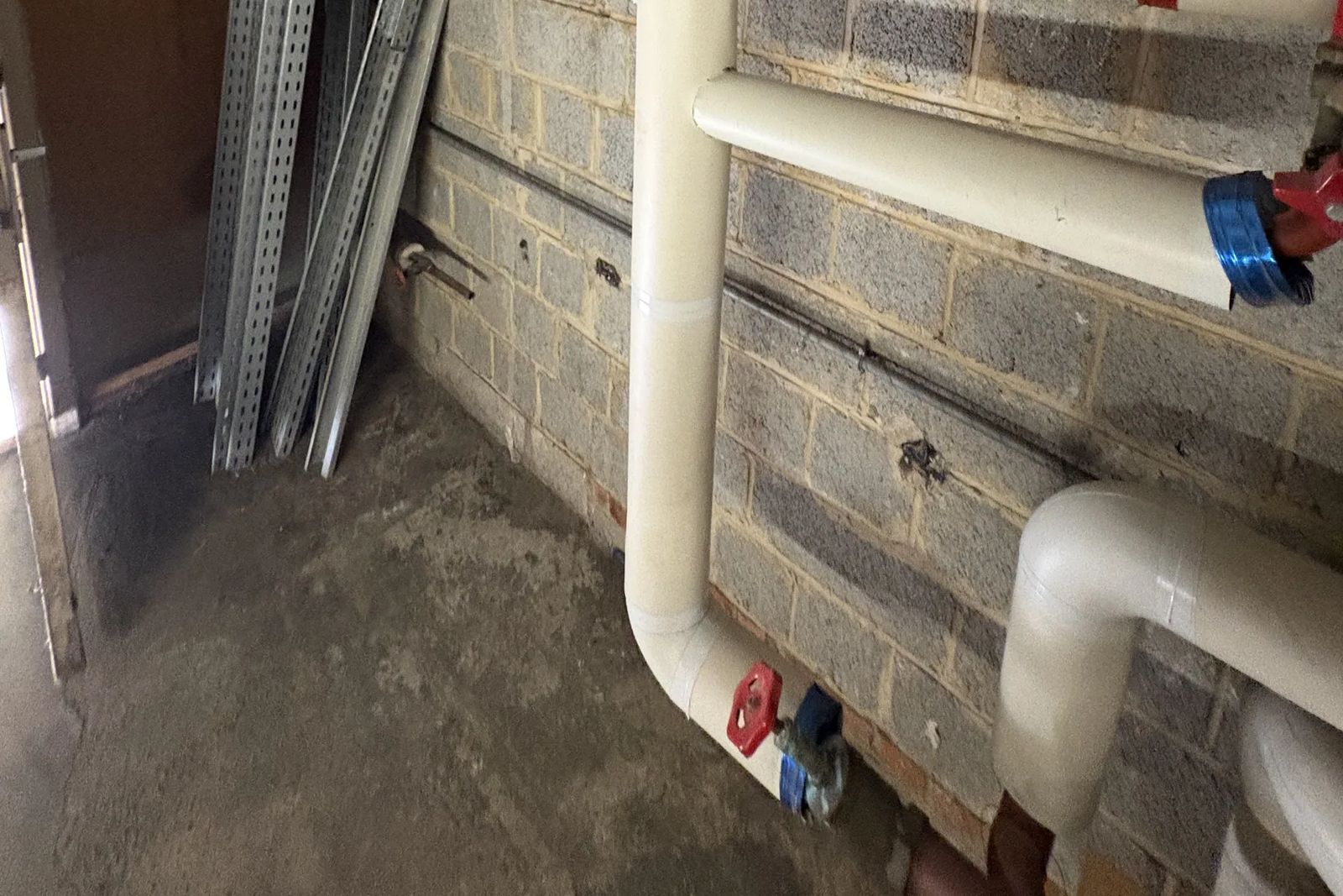 White insulated pipes running down a block wall to the floor