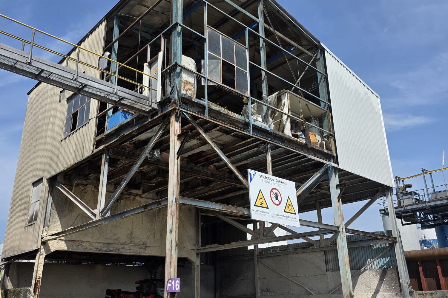 Industrial building on a steel frame with a warning sign, its cladding being removed
