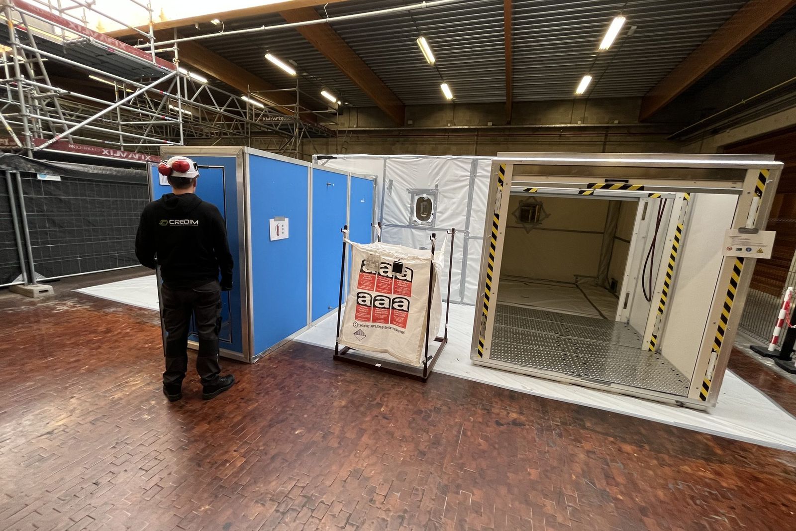 Montage d'une zone hermétique dans un hall au sol en parquet, avec une cabine en panneaux bleus