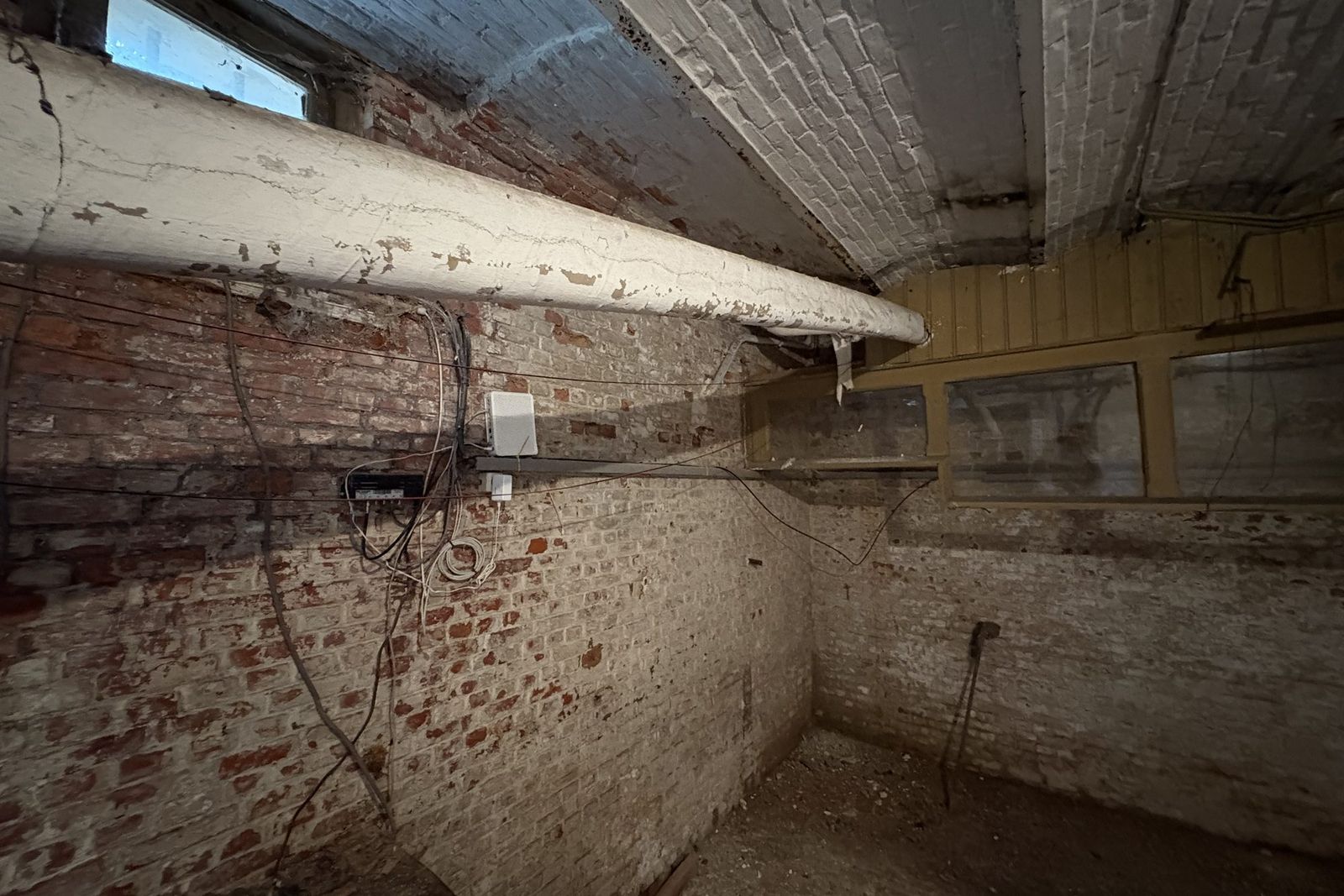Basement with a long insulated pipe under the brick ceiling