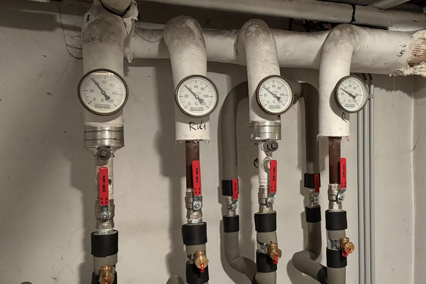 Thermomètres et vannes à poignée rouge sur des conduites verticales isolées