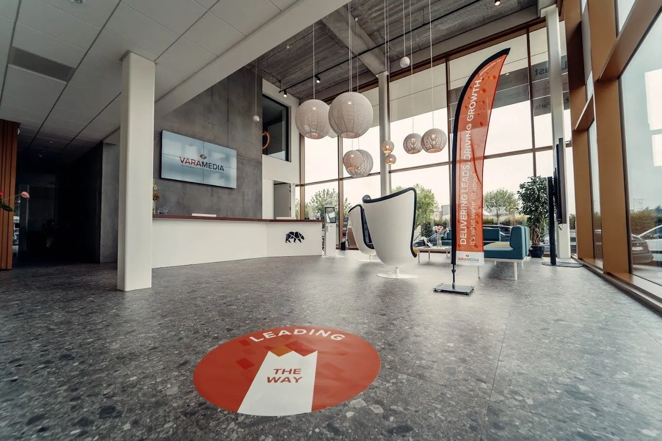 Moderne kantoorlobby met 'Leading the Way' vloersticker en oranje beachvlag