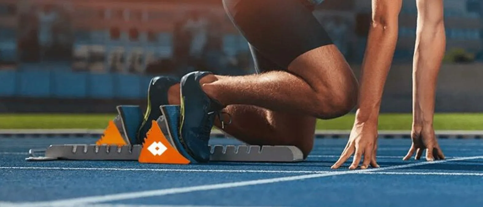 Atleet in startblokken klaar voor sprint op blauwe atletiekbaan