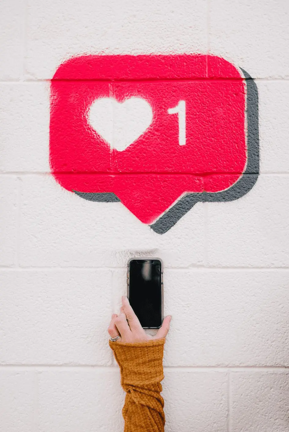 Hand houdt smartphone vast onder geschilderd Instagram like-icoon op muur